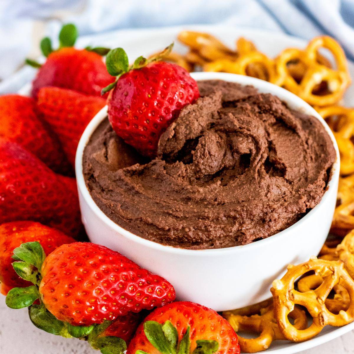Bowl of chocolate hummus with strawberries and pretzel twist.