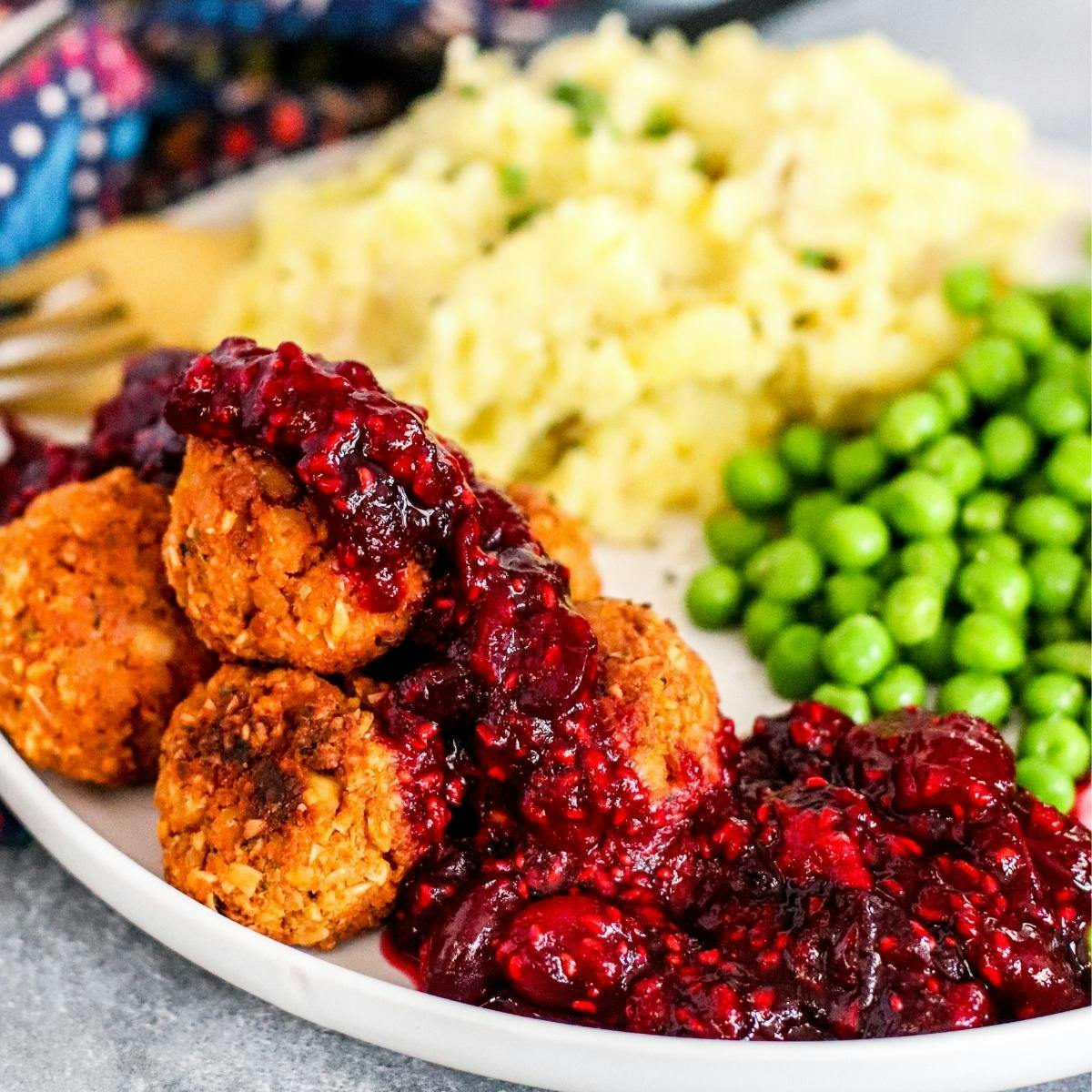 Tofu meatballs topped with cranberry sauce, mashed potatoes, and peas on a dinner plate.