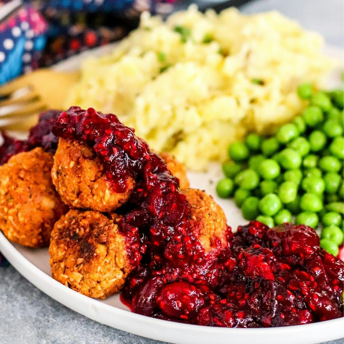 A plate of tofu meatballs with cranberry sauce, mashed potatoes, and peas.