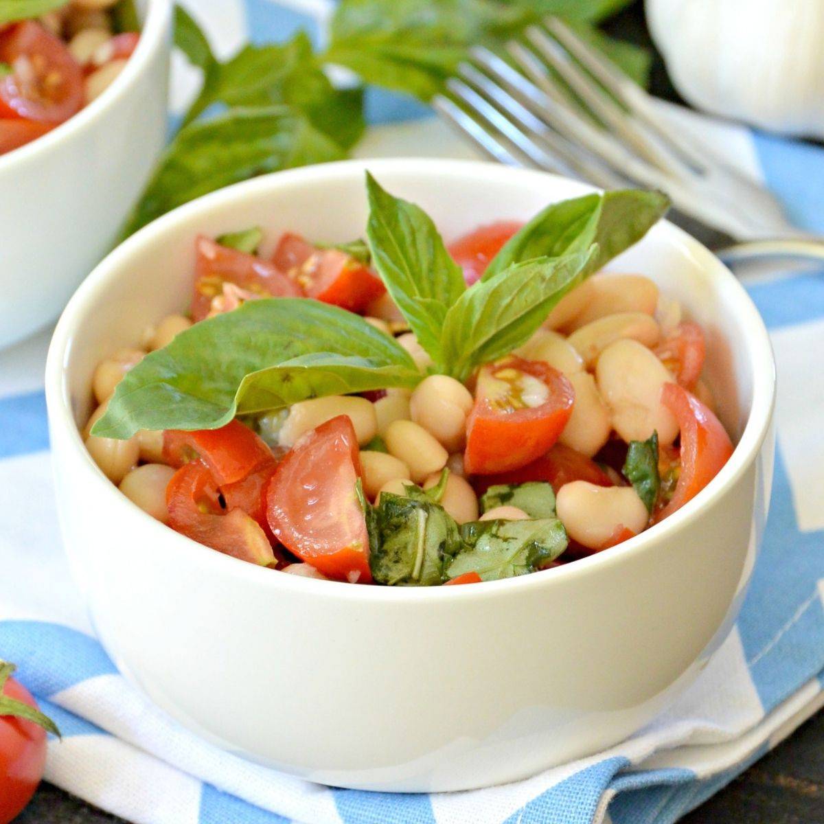 Bowl of cherry tomato and white bean salad topped with fresh basil.