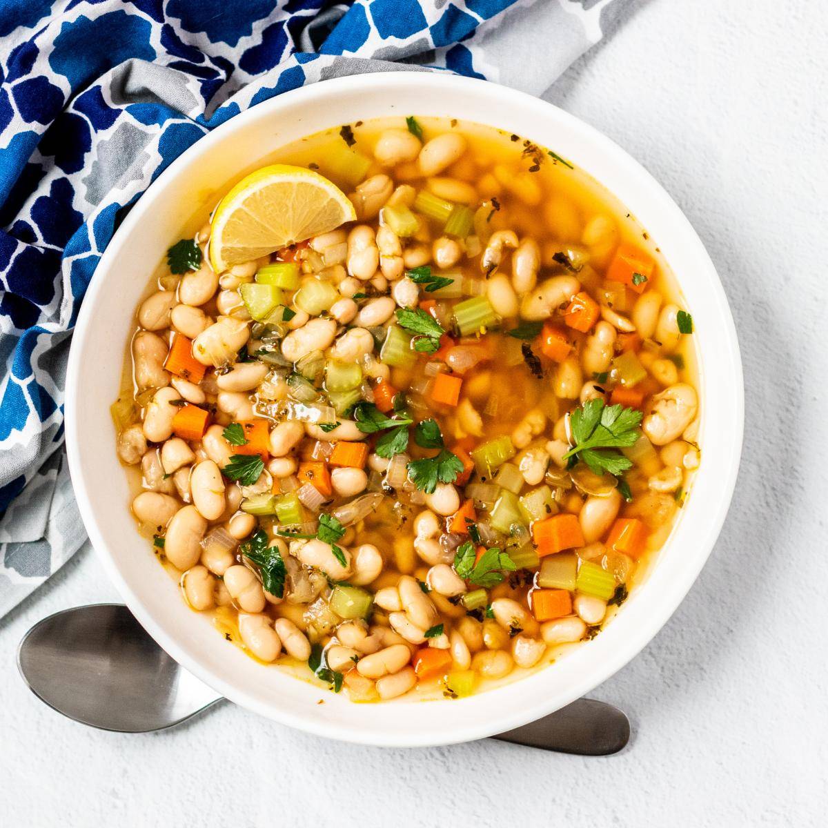 Bowl of Mediterranean white bean soup garnished with a lemon wedge.