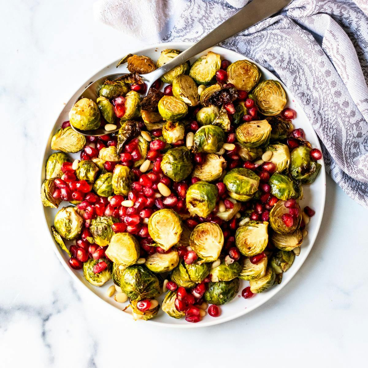 Plate of roasted Brussels sprouts with pomegranate seeds and pine nuts.