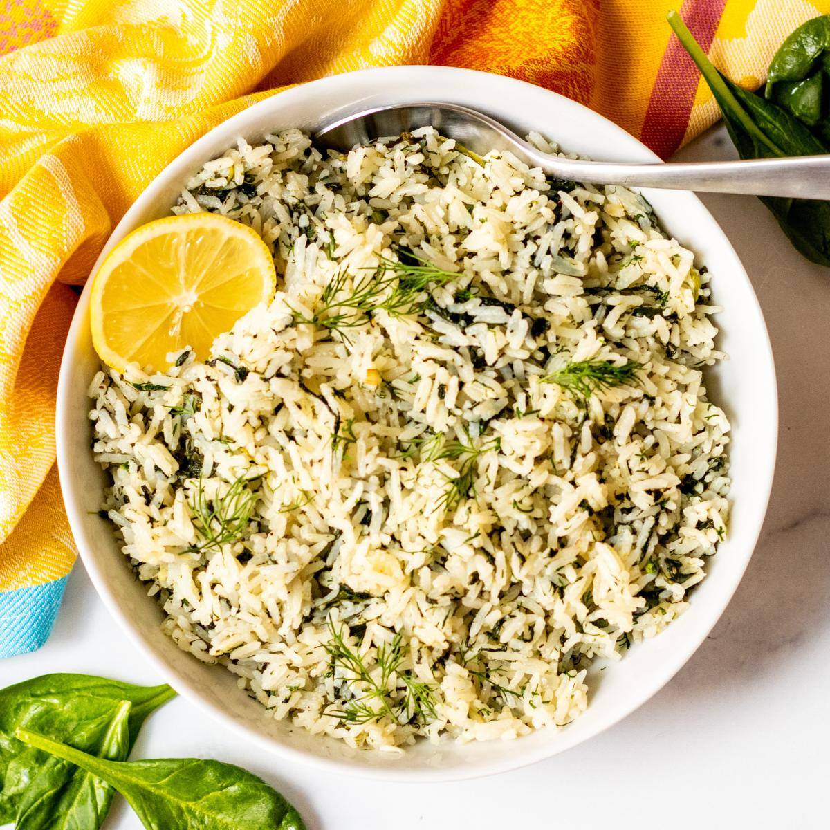 Bowl of spinach rice garnished with fresh dill and a slice of lemon.