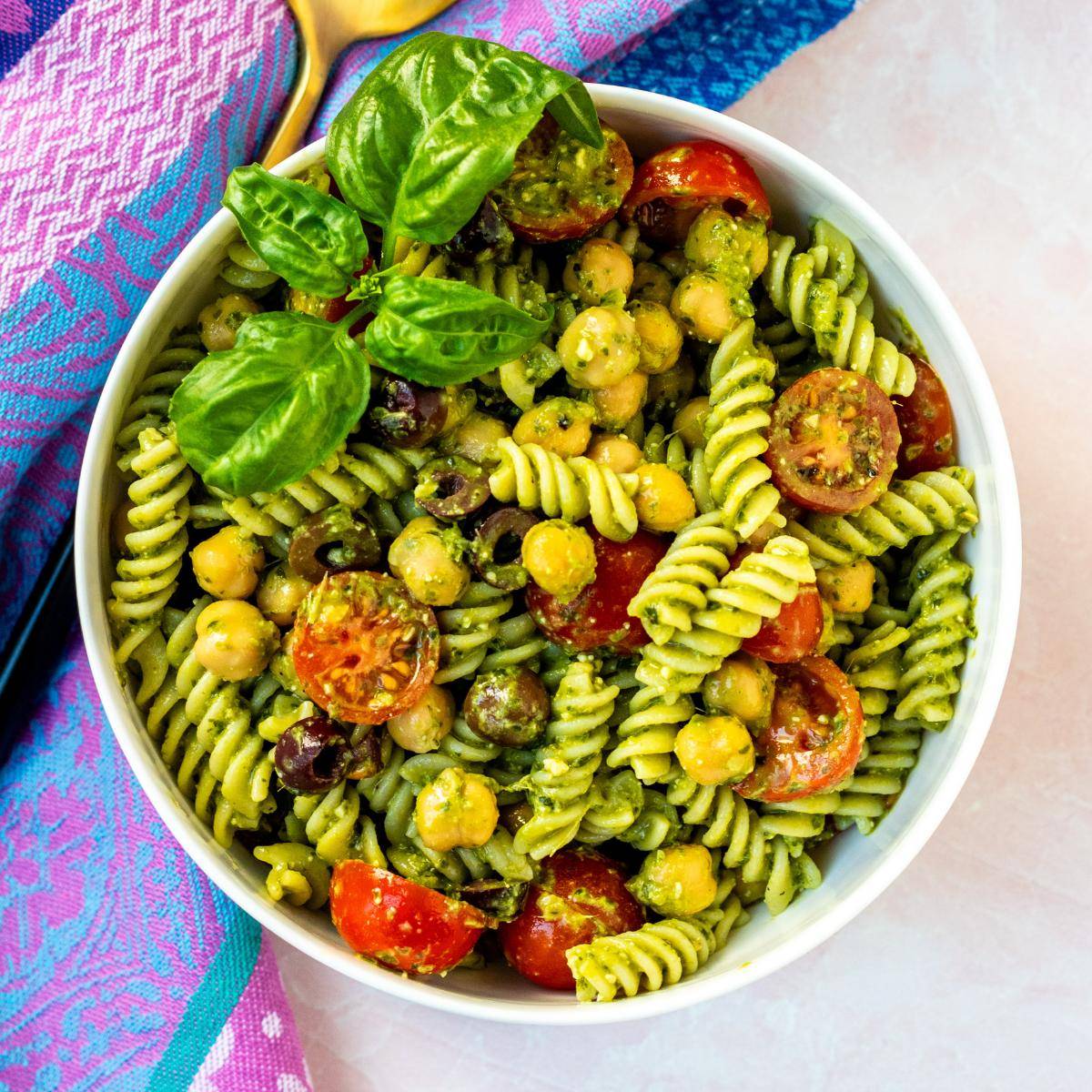 Bowl of pesto pasta salad with chickpeas, tomatoes, and olives.
