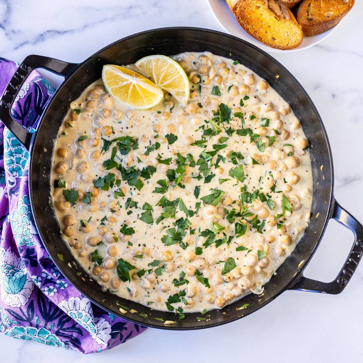 Lemon pepper chickpeas with cashew cream in a skillet garnished with lemon wedges and fresh parsley.