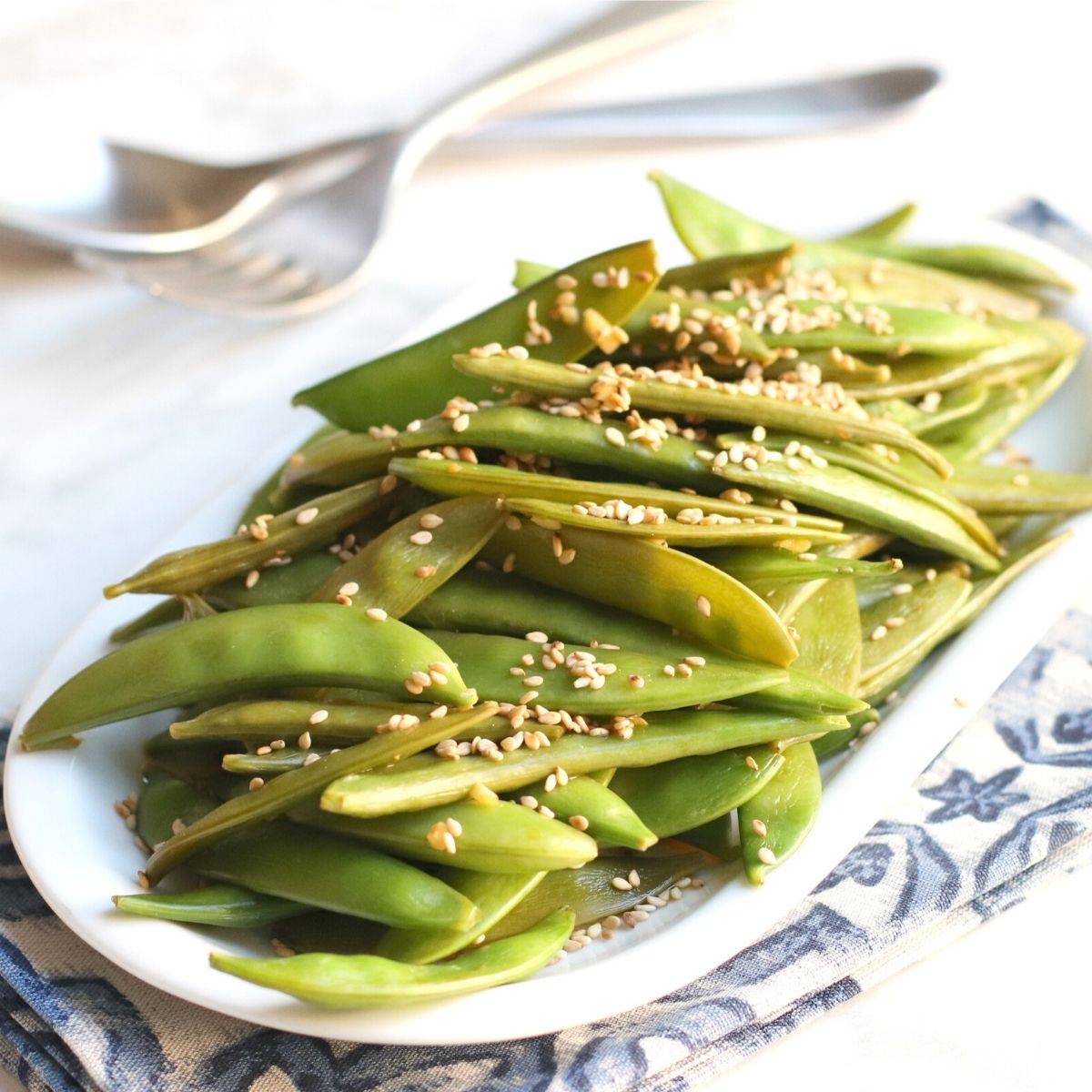 Platter of sauteed sugar snap peas garnished with sesame seeds.