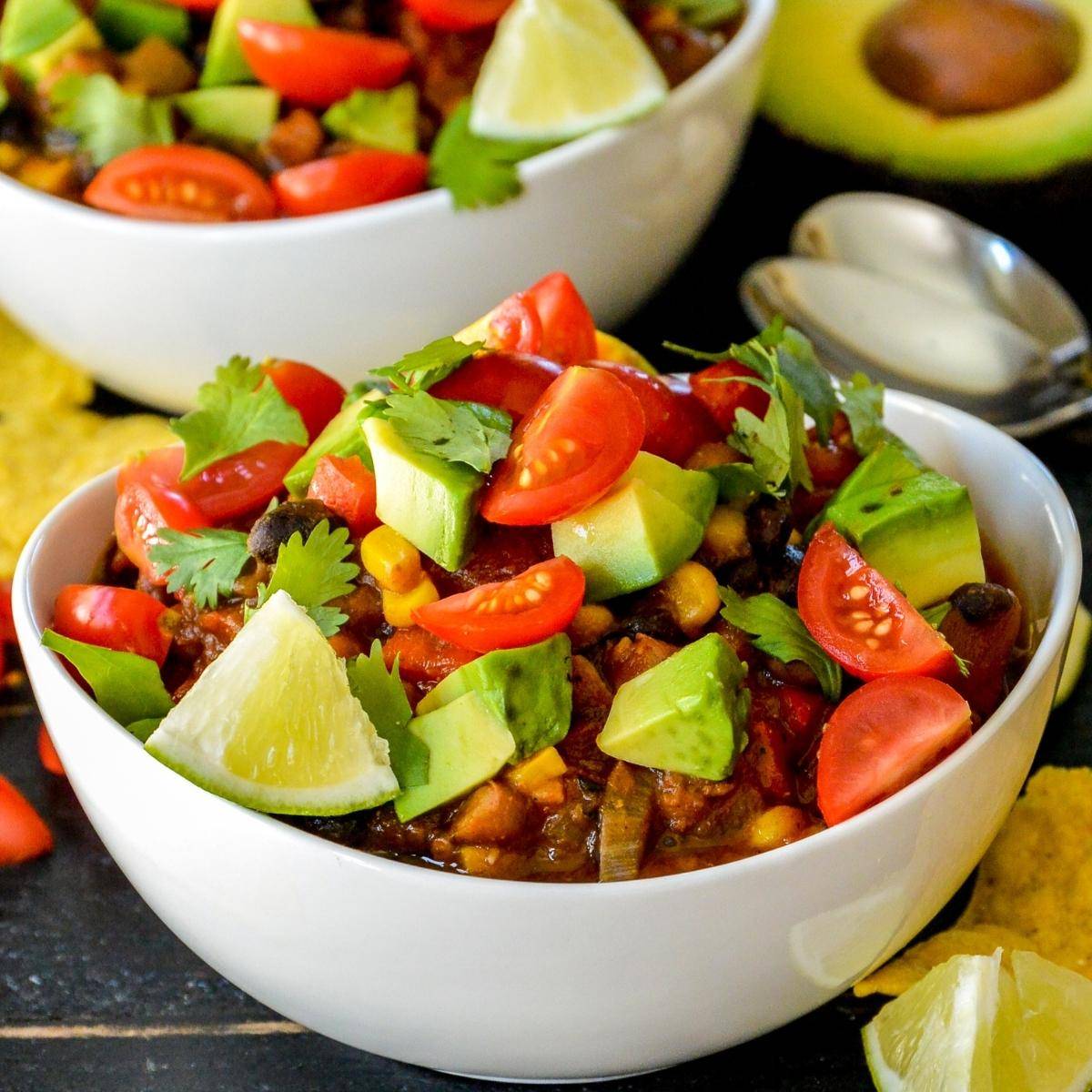 Bowls of pumpkin chili topped with tomatoes, avocado, and cilantro.