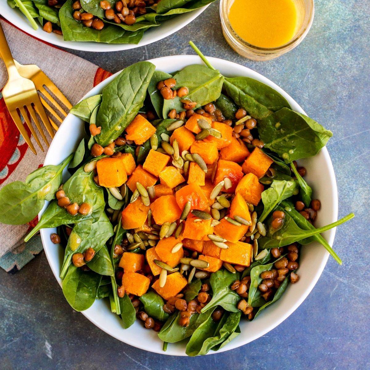 Bowl of spinach salad with roasted butternut squash cubes, lentils, and pumpkin seeds.