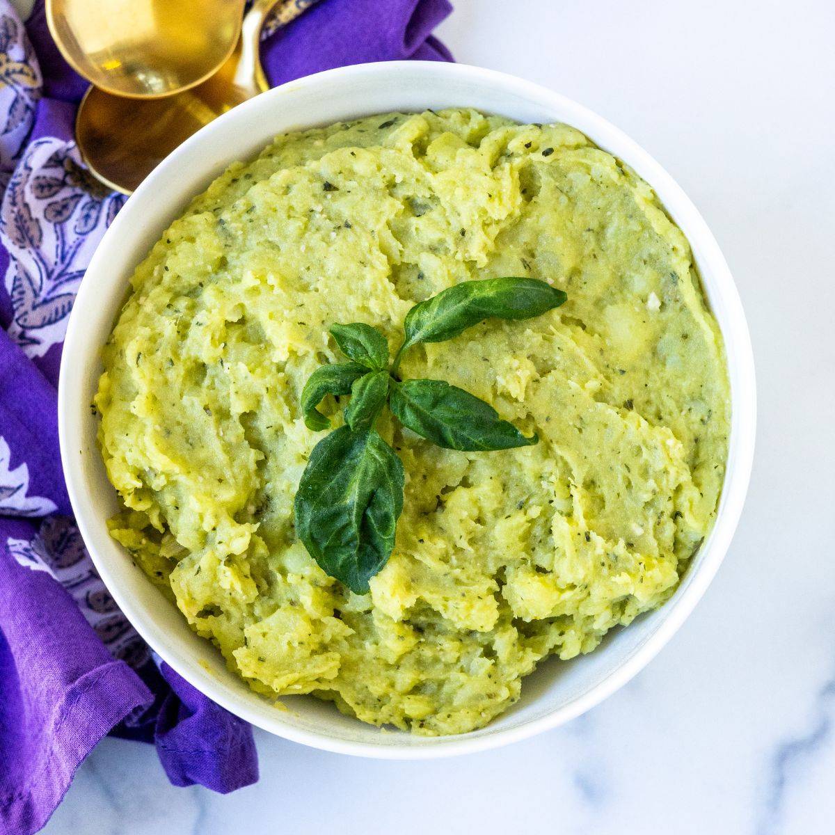 Bowl of pesto mashed potatoes garnished with a sprig of basil.