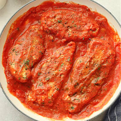 Chicken breasts in tomato sauce in a white skillet.