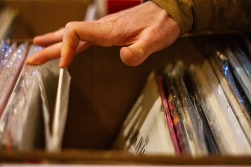 A hand sifting through a box of vinyl records