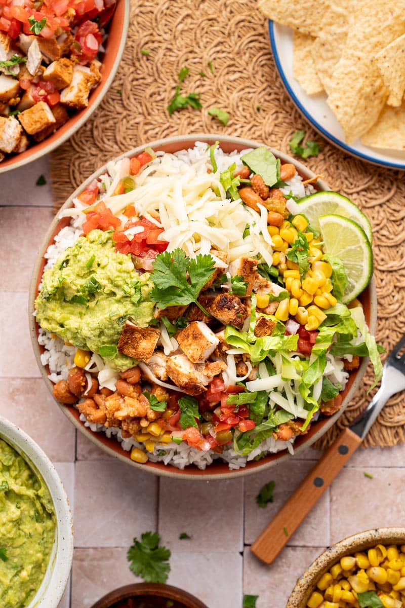 chipotle chicken burrito bowls with shredded cheese, corn, lettuce, lime 