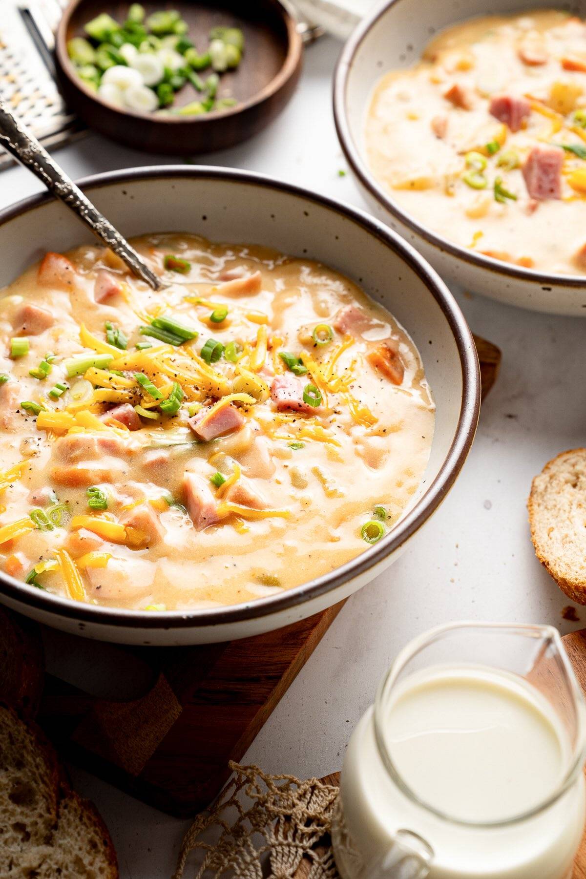 bowl with ham and potato soup garnished with shredded cheddar and green onions