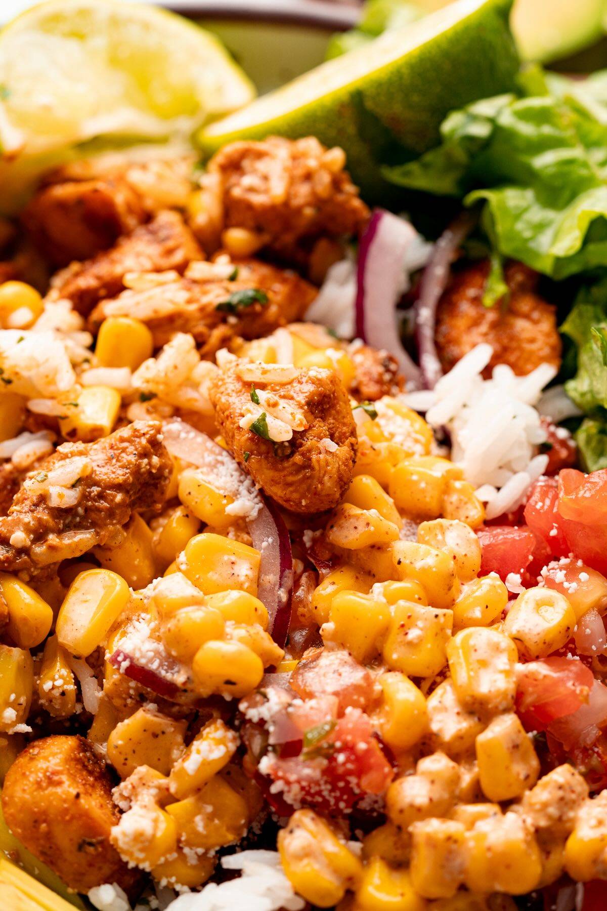 street corn chicken rice bowl with chicken, corn, rice, lettuce, avocado, and lime wedges