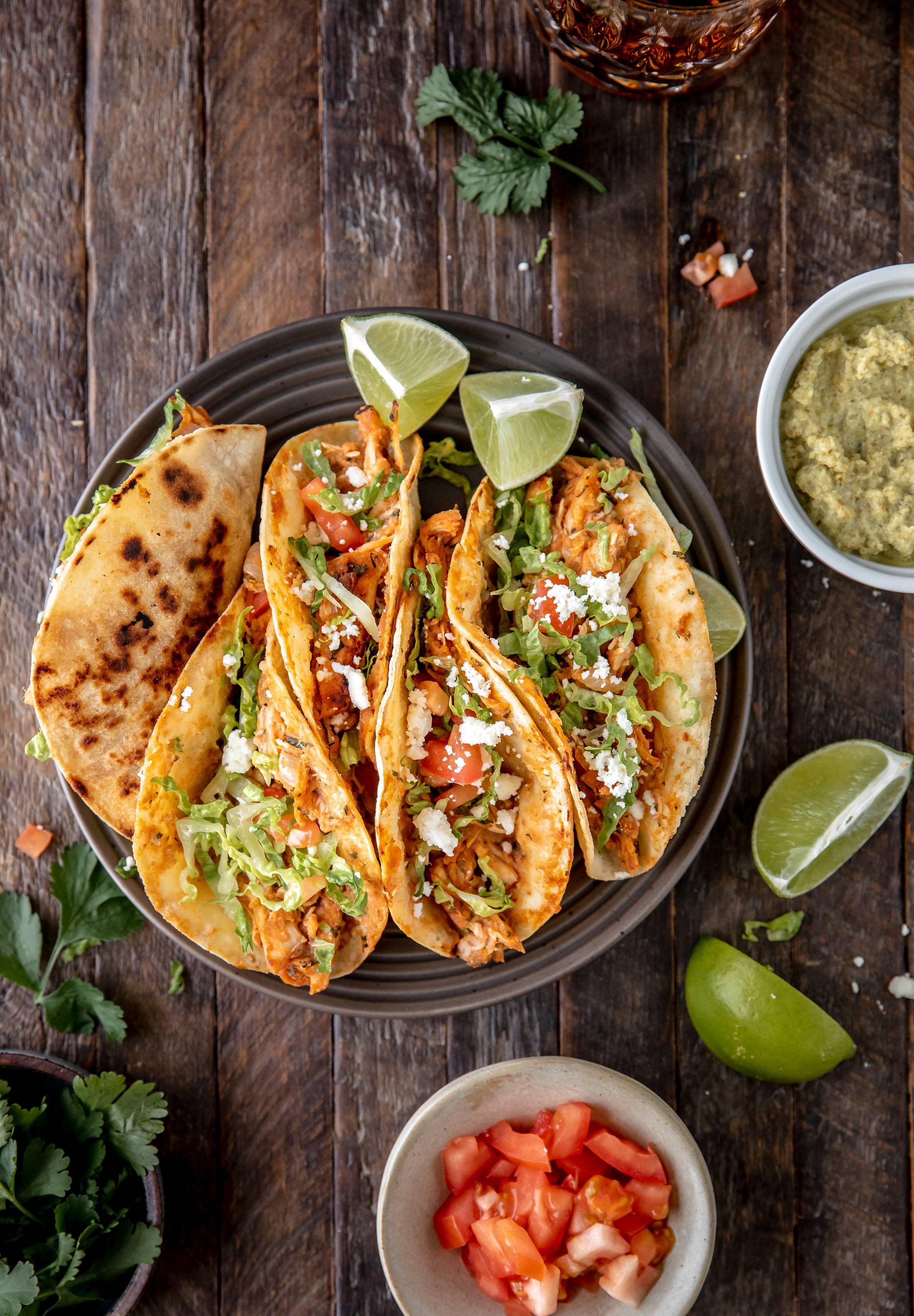 chicken street tacos topped with lettuce and cojita with limes on the side
