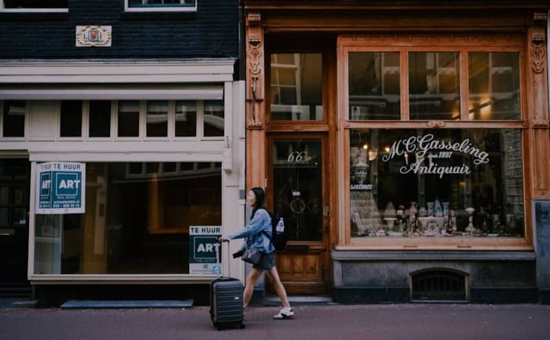 woman walking with suitcase next to storefronts