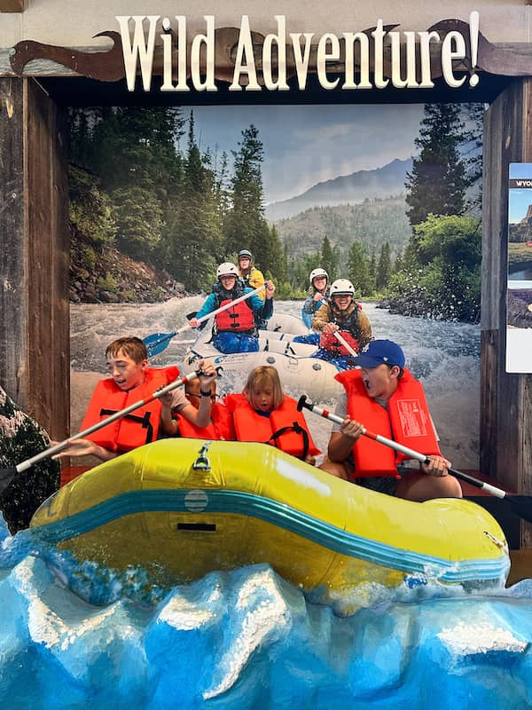 Four boys pretending to whitewater raft in an interactive display at a Wyoming visitor center.