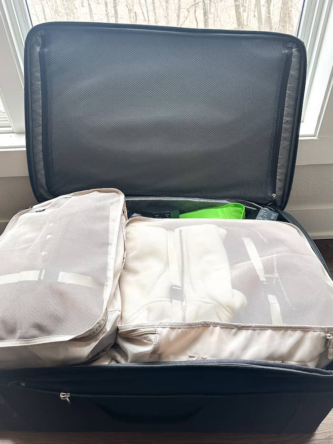 Black suitcase open with mesh beige colored packing cubes in it.