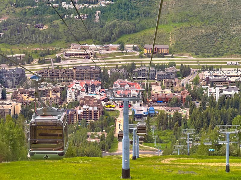 View from a gondola descending toward Vail’s Lionshead Village, showing mountain slopes, green trees, and alpine-style buildings below.