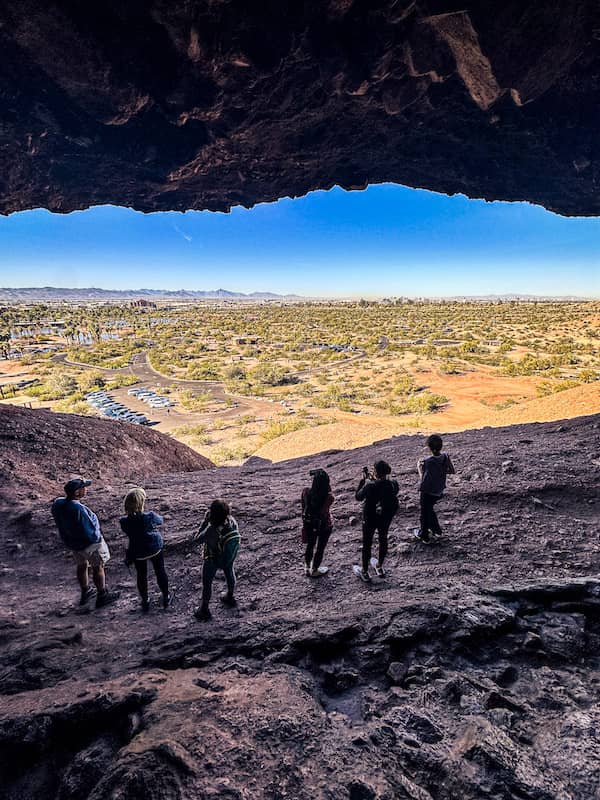 People standing inside Hole in the Rock at Papago Park with panoramic views of the desert and city below