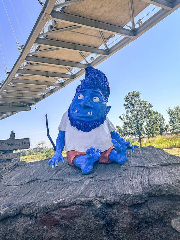 A large blue Troll statue sitting on a boulder under the Bob Kerrey Pedestrian Bridge in Omaha, Nebraska