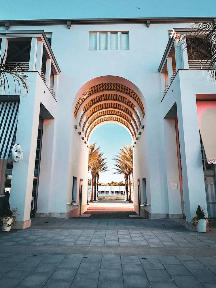 A white stucco looking building with an barrel ceiling walkway to a grassy area with palm trees in Seaside, Florida.