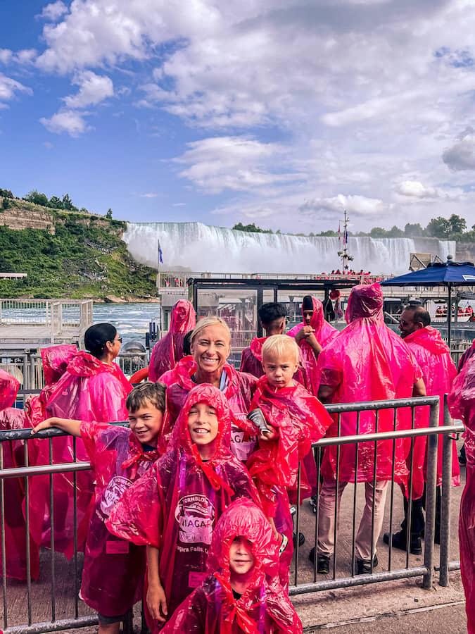 Mom with her sons wearing pink ponchos standing on the Niagara City Cruises boat with Niagara Falls in the background.