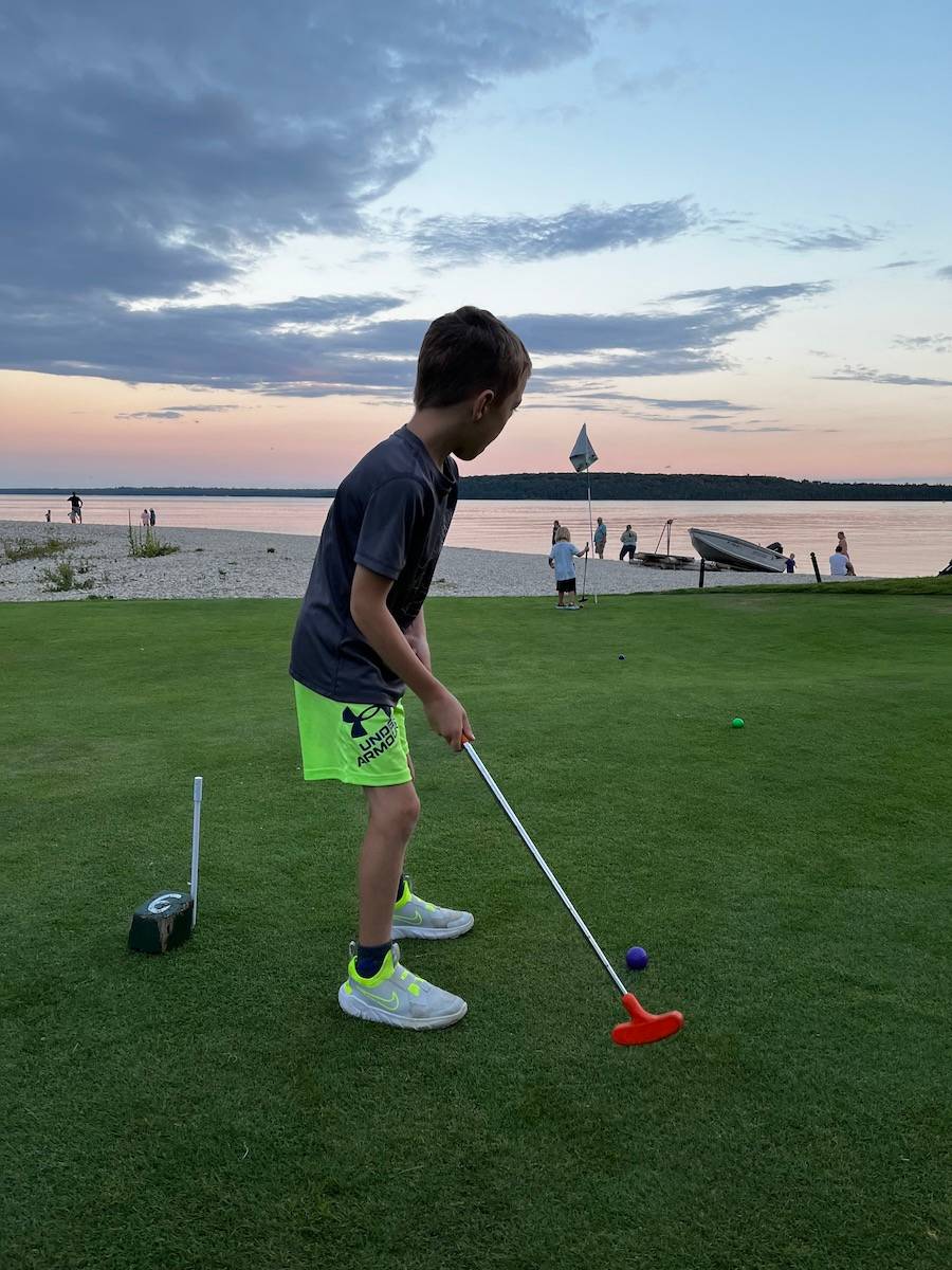 Young boy playing miniature golf at Mission Point Resort on Mackinac Island as the sun is setting.