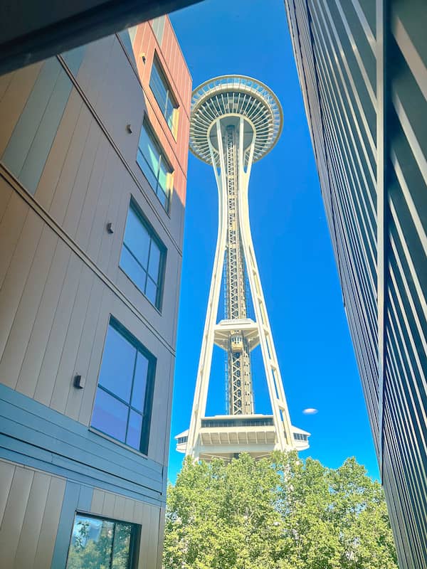 View of the Seattle Space Needle seen through a hallway window at the Hyatt House, framed between two buildings on a clear day.