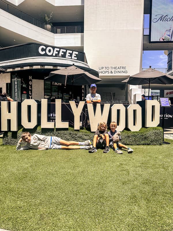 Four boys posing in front of a Hollywood sign display at Ovation Hollywood in Los Angeles, California, during a family vacation.