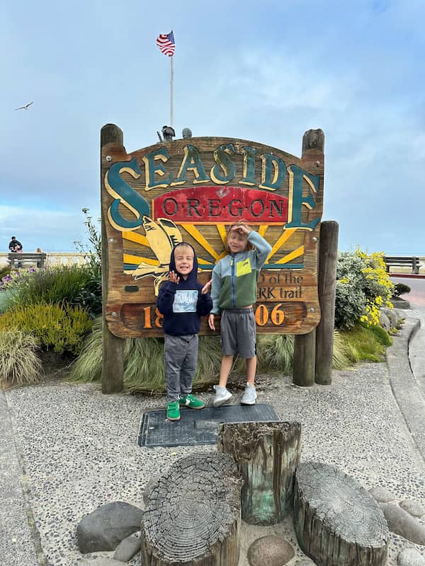 Two young boys standing in front of the Seaside, Oregon end of the Lewis and Clark Trail sign at the Seaside Turnaround.