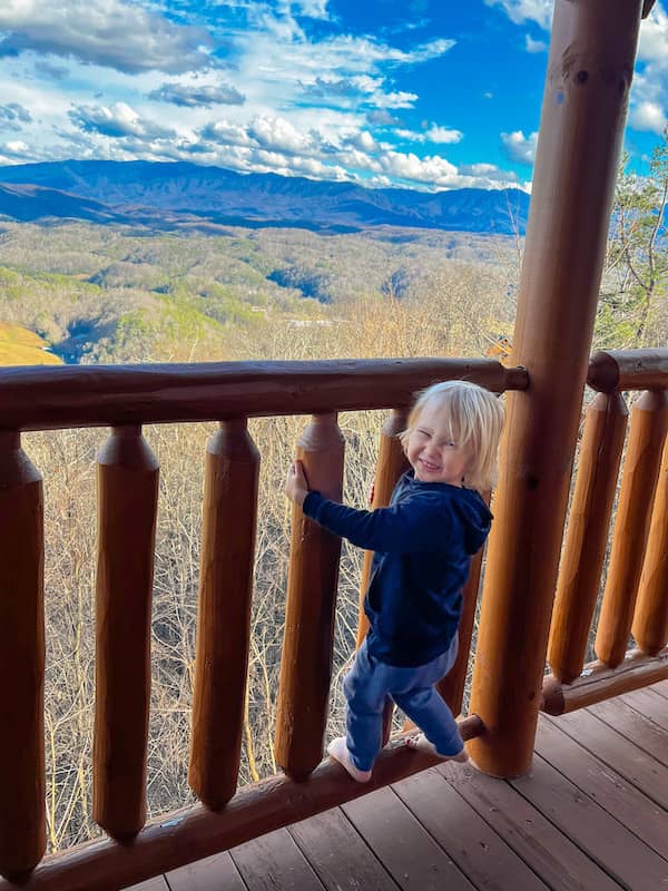 A boy holding onto a railing at a vacation rental with an unobstructed view of the Great Smoky Mountains and sky in the background.