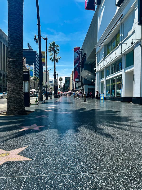 Hollywood Walk of Fame along Hollywood Boulevard in Los Angeles, California, with palm trees, star-lined sidewalks, shops, and visitors walking on a sunny day.