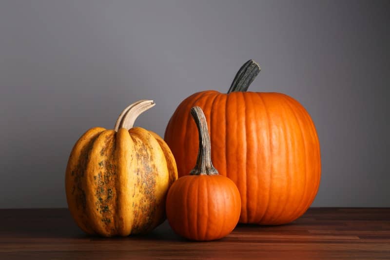 3 pumpkins sitting on top of a wooden table