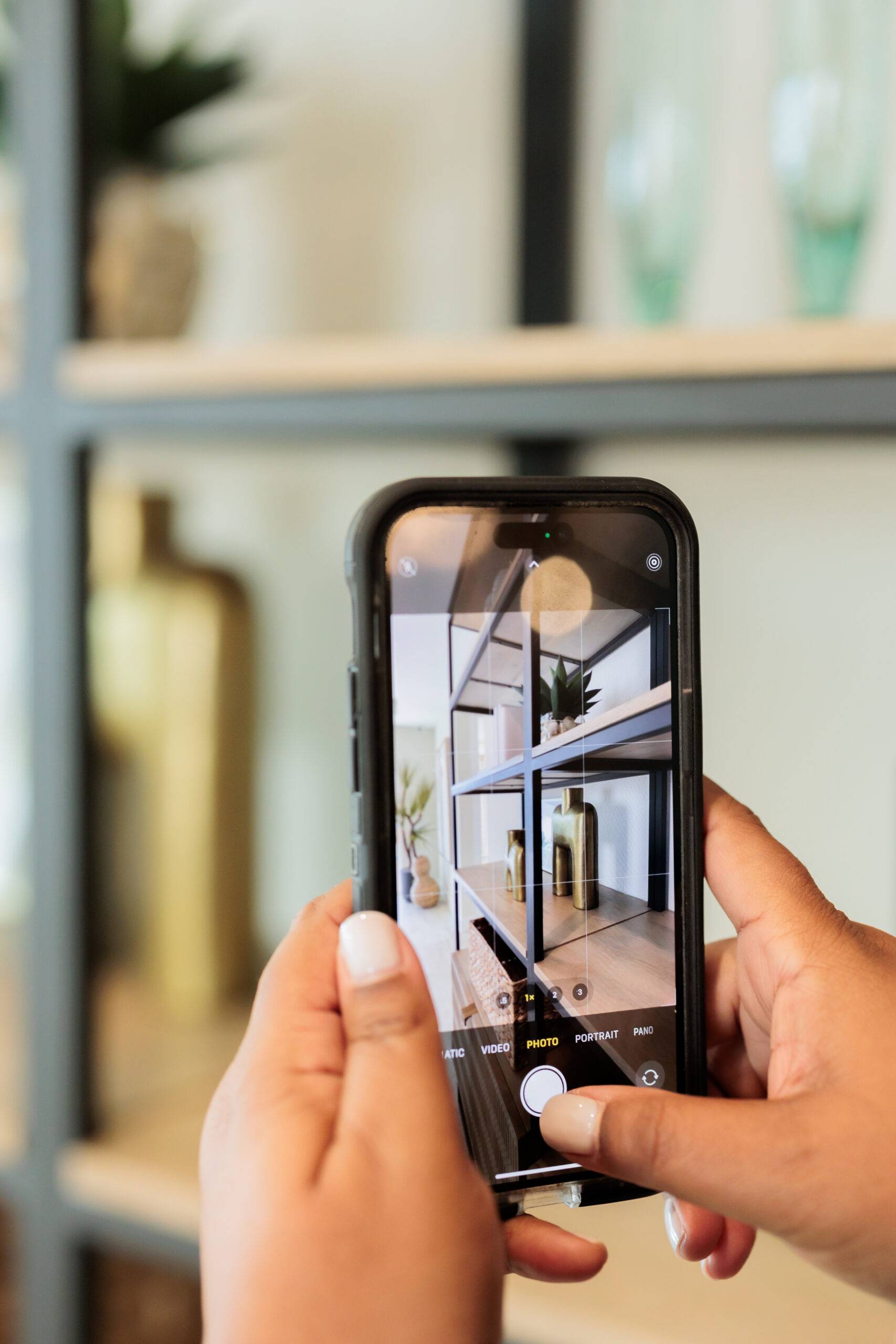 Hands holding a smartphone to photograph a styled shelf for an Instagram post