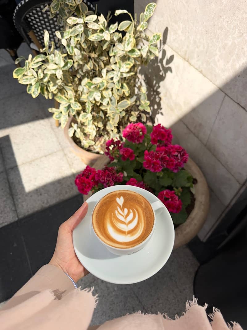 Latte art coffee cup held by hand with flowers.