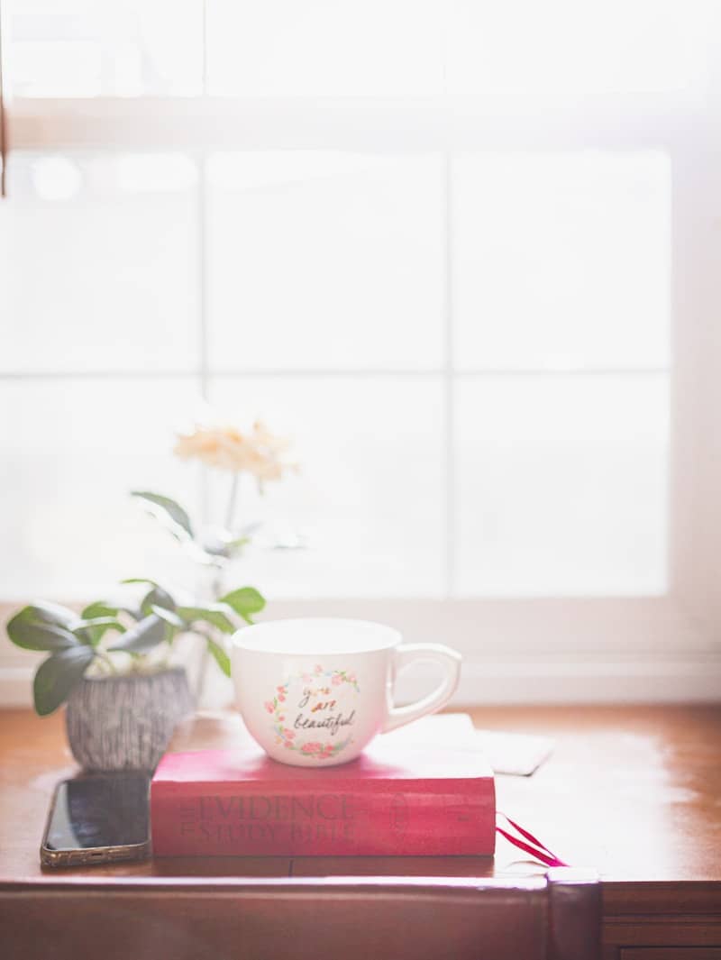 Mug with flowers sits on a book by window