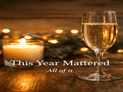 A softly lit New Year’s Eve scene with a champagne flute and glowing candle on a wooden table, overlaid with the words “This Year Mattered. All of it.” conveying reflection, gratitude, and quiet celebration.