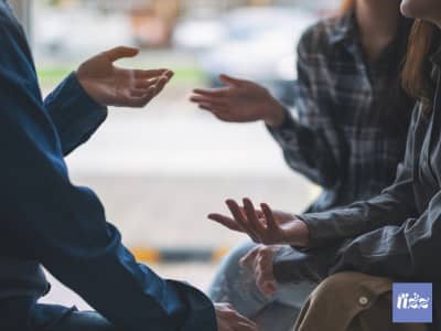 lose-up of a small group of women gesturing with their hands during an animated, engaged conversation, seated close together outdoors.