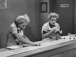 Black-and-white image of Lucy and Ethel in a factory kitchen standing beside a convey