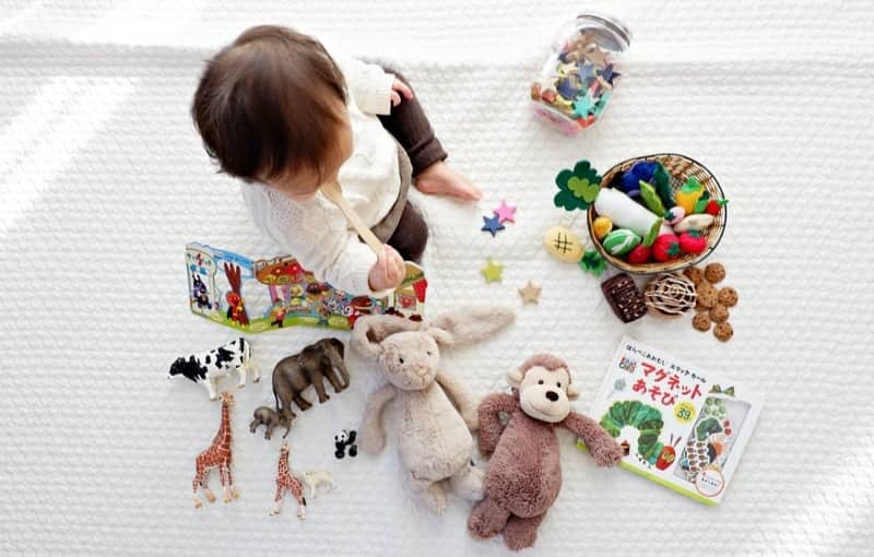 boy sitting on white cloth surrounded by toys