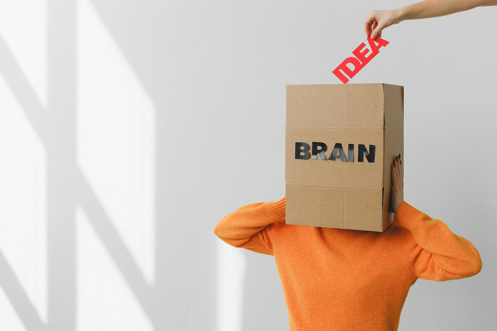Person with a box (with "BRAIN" written on it) as a head and someone taking the letters "IDEA"  out of the box