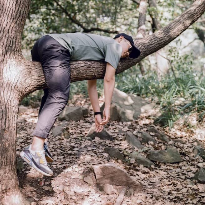 man in black t-shirt and blue denim jeans sitting on tree branch