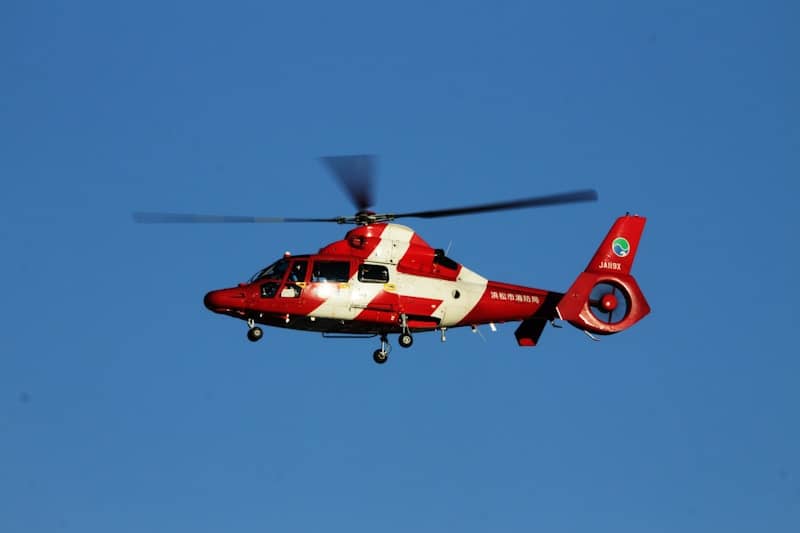 Red and white helicopter flying against a blue sky.