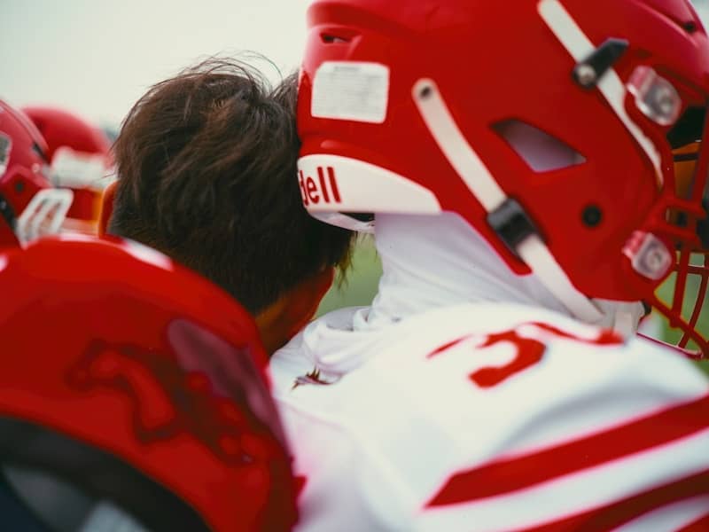 American football players in red helmets huddle together.