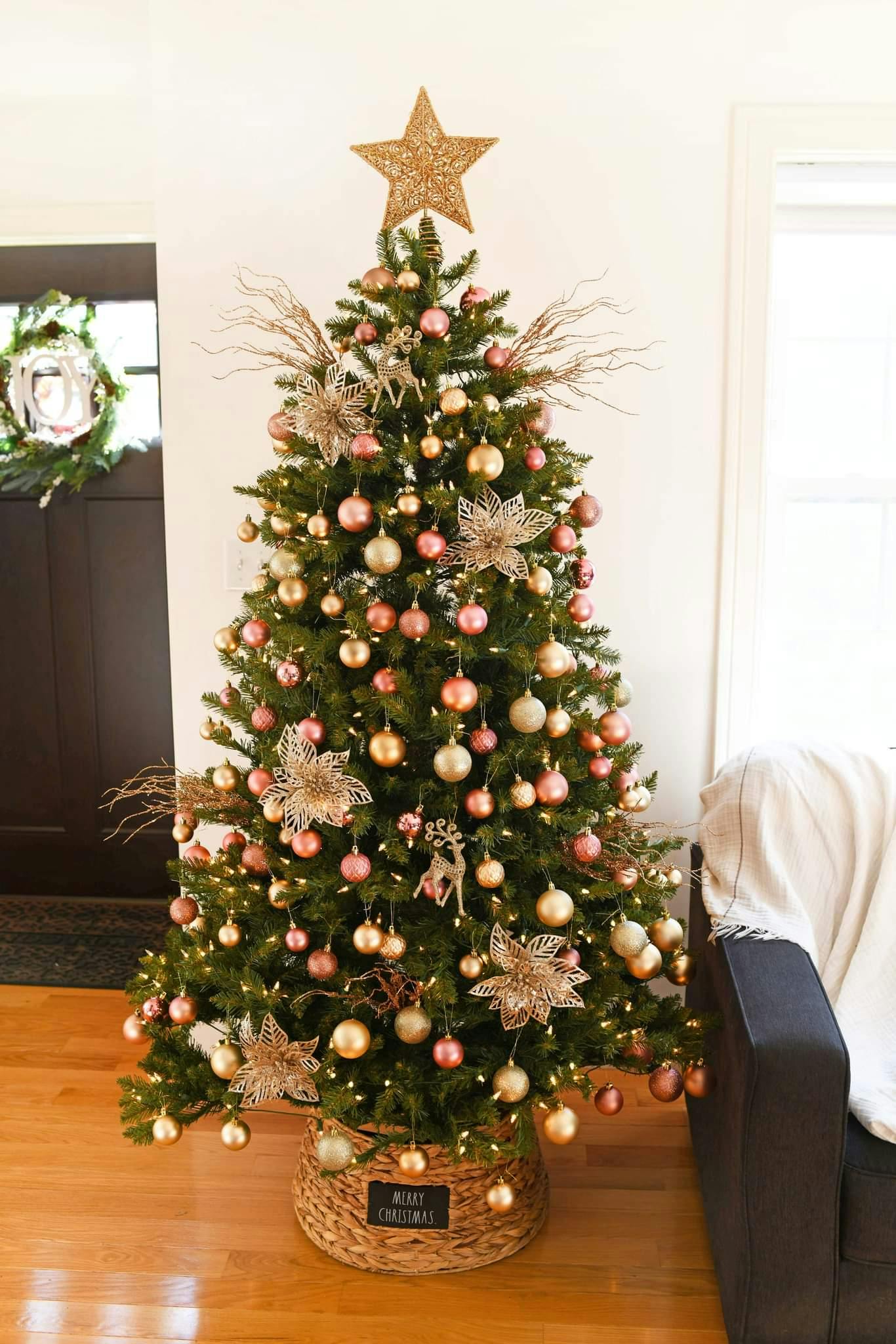 Christmas tree decorated with rose gold and pink ornaments in a home with wood floor.