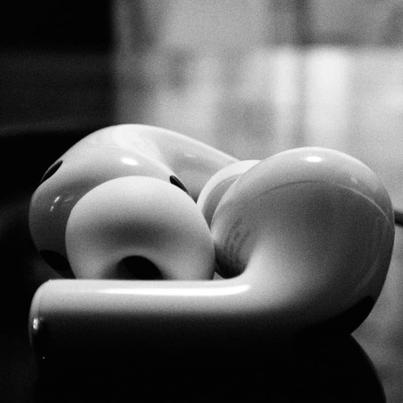 Two white wireless earbuds resting on a dark reflective surface in black and white