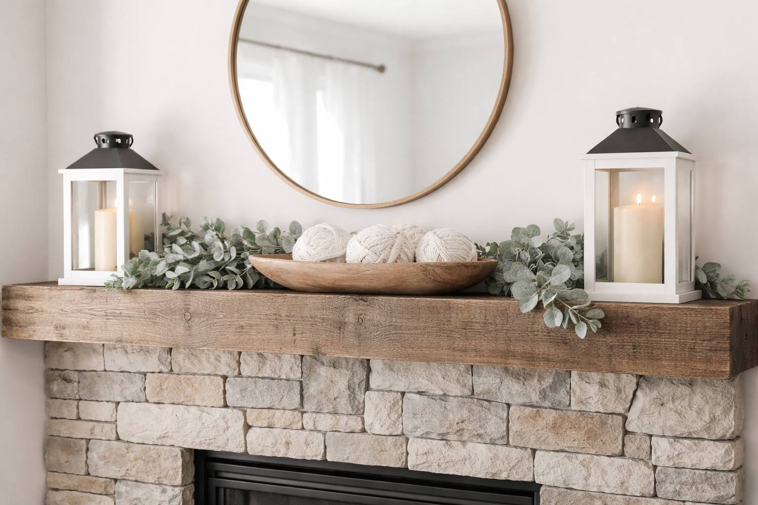 modern fireplace mantle with cozy winter eucalyptus leaves white lanterns with candles, and a wood bowl with white yarn.