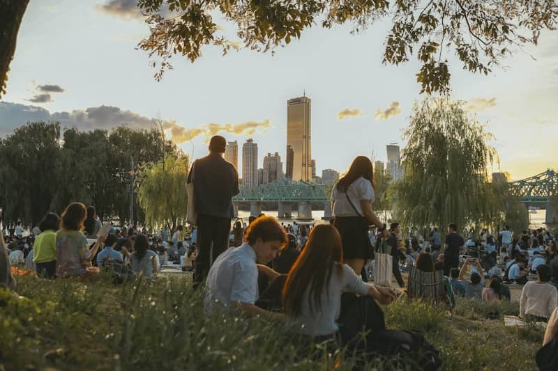 People relax in a park with city skyline at sunset.