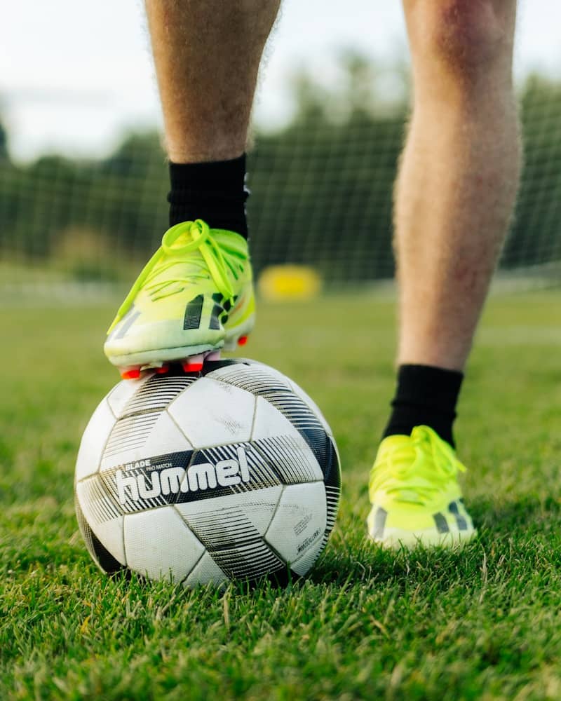 Cleated foot on a soccer ball on green grass.